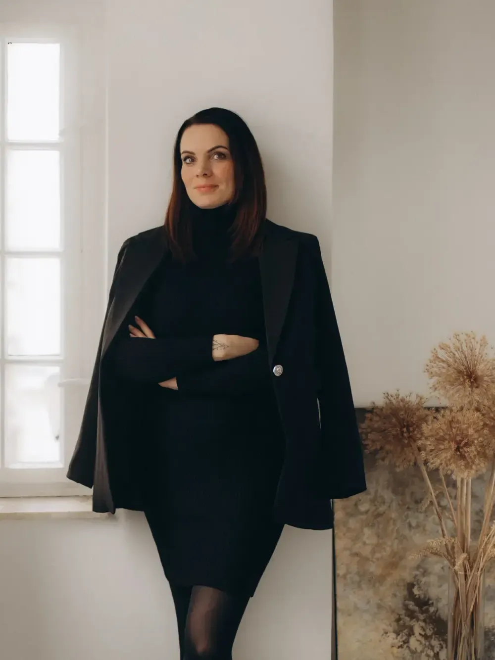 Mandy Schaak, Gründerin von MM Brandspace, lehnt in schwarzem Blazer an einer hellen Wand vor einem Fenster